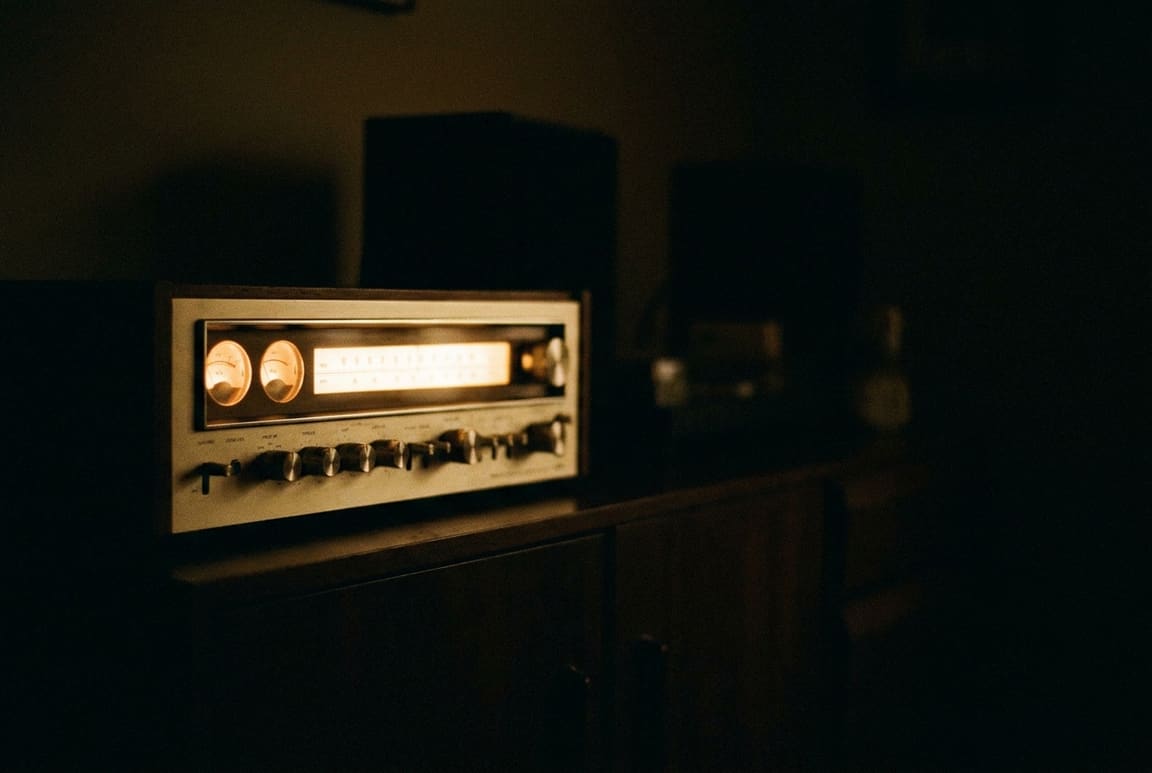 A 1970s cream-and-walnut stereo receiver with twin VU meters and a lamplit tuning dial in a dark room